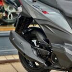 Close-up van de achterzijde van een grijze scooter met uitlaat, achterwiel en zadel.