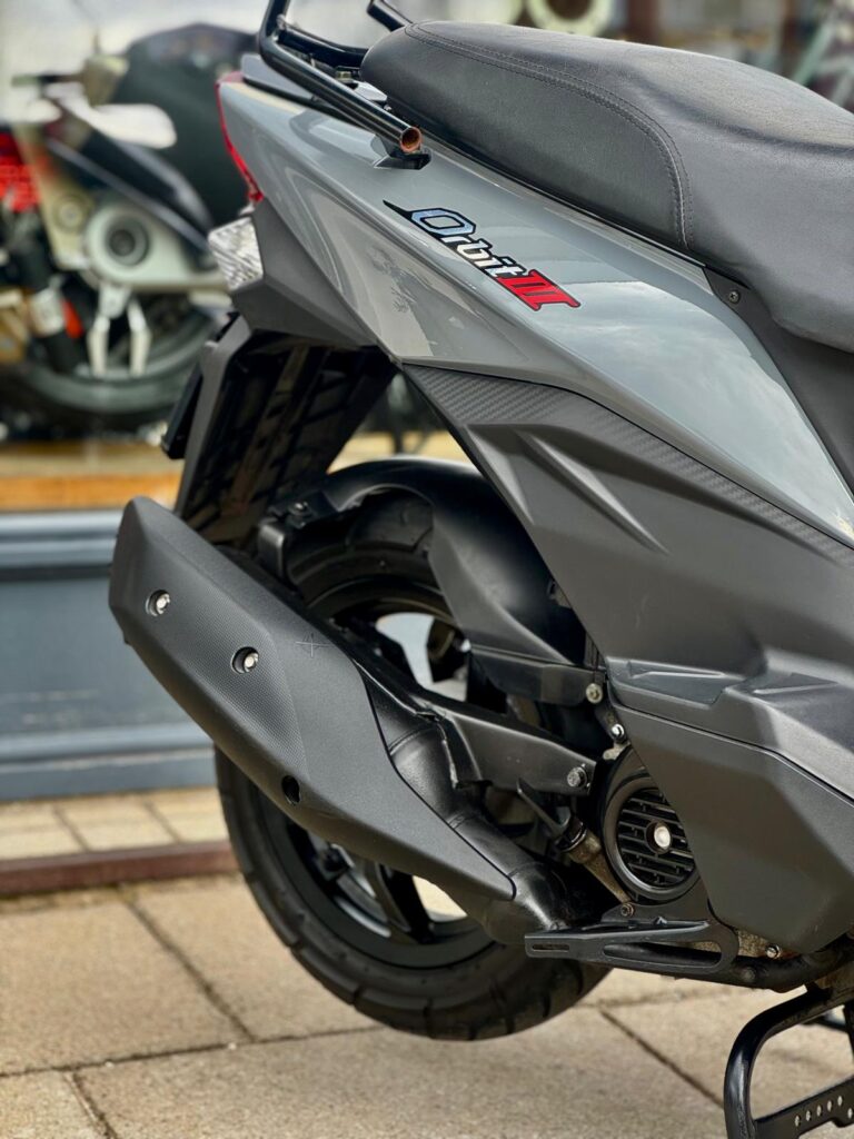 Close-up van de achterzijde van een grijze scooter met uitlaat, achterwiel en zadel.