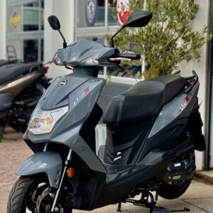 Grijze scooter op de standaard met schijfrem, geparkeerd voor een showroom met logo's.