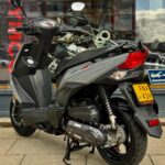 Grijze scooter op middenbok voor een winkelruit, met zichtbaar Nederlands kenteken.