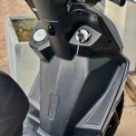 Close-up van het stuur en de voetenplank van een zwarte scooter met sleutel in het contact.