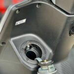 Close-up van open brandstofklep en tankdop van scooter met E5-sticker.