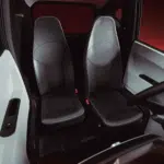 Twee zwarte, smalle autostoelen naast elkaar in een compacte cabine met donker interieur.