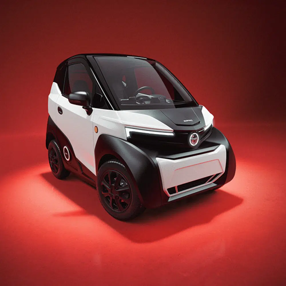 Wit-zwarte elektrische microauto in studio, driekwart vooraanzicht op rode achtergrond.