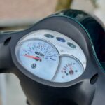 Close-up van het dashboard van een scooter met snelheidsmeter en brandstofmeter.