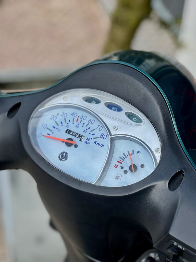 Close-up van het dashboard van een scooter met snelheidsmeter en brandstofmeter.