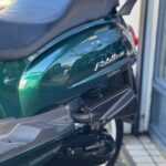 Close-up van de achterkant van een groene scooter met zwart zadel en witte velg.