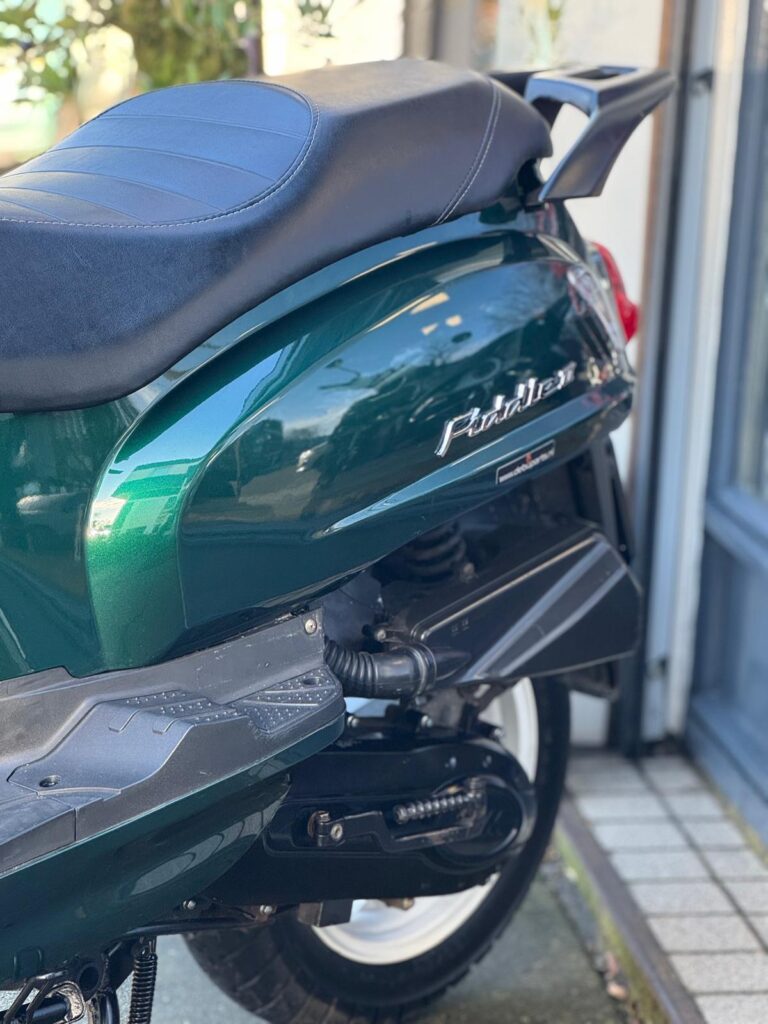 Close-up van de achterkant van een groene scooter met zwart zadel en witte velg.