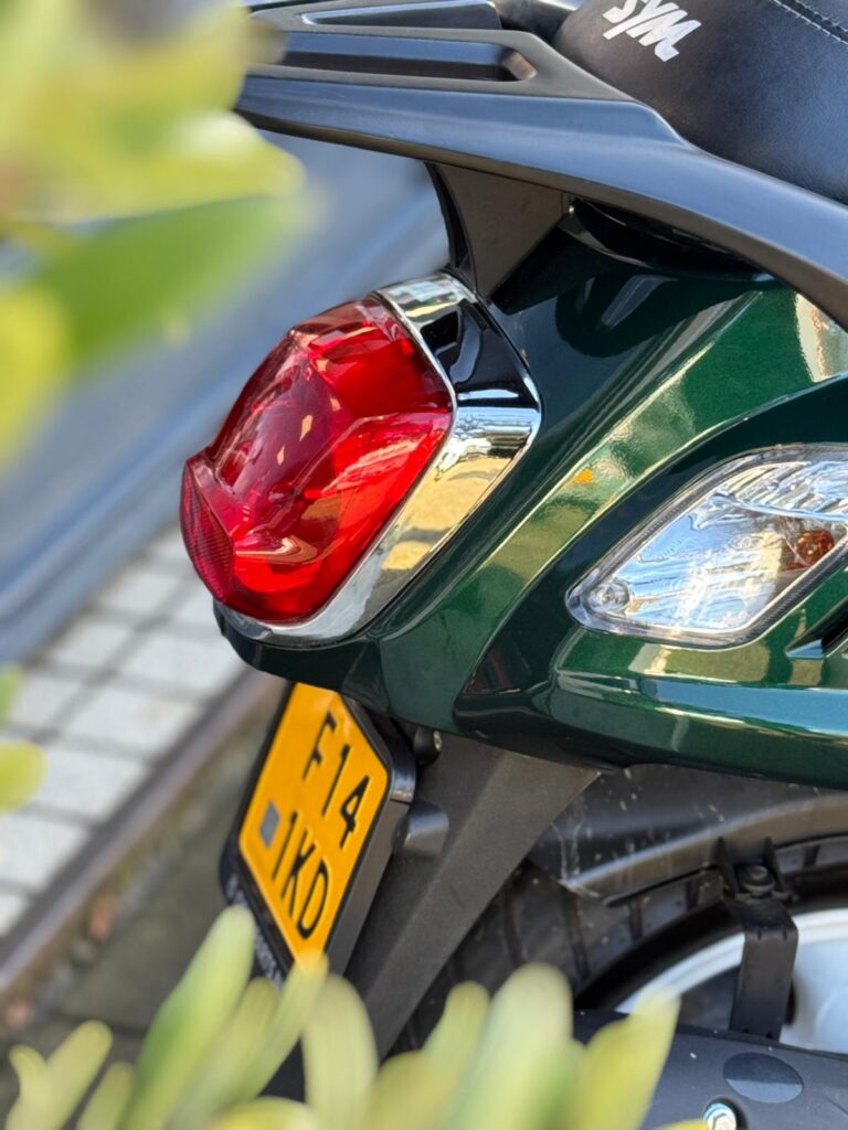 Close-up van de achterzijde van een groene scooter met rood achterlicht en gele kentekenplaat.