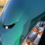 Close-up van de metallic groene voorkant van een scooter met koplamp en oranje knipperlichten.