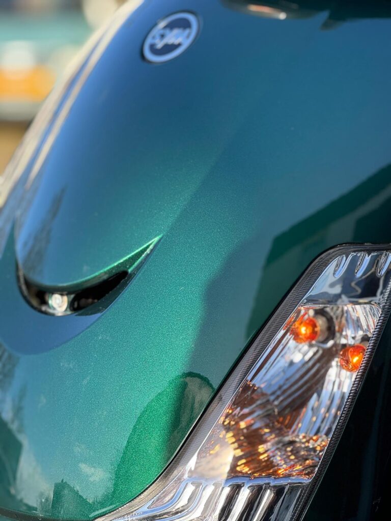 Close-up van de metallic groene voorkant van een scooter met koplamp en oranje knipperlichten.
