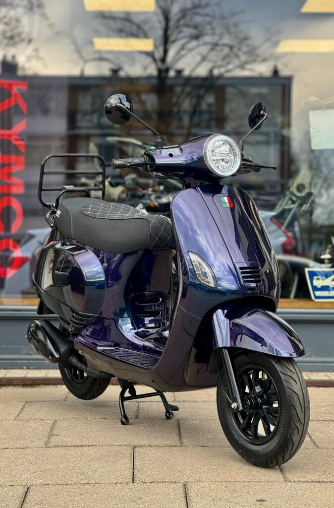 Paars metallic retro scooter met ronde koplamp en bagagedrager voor een winkelraam.