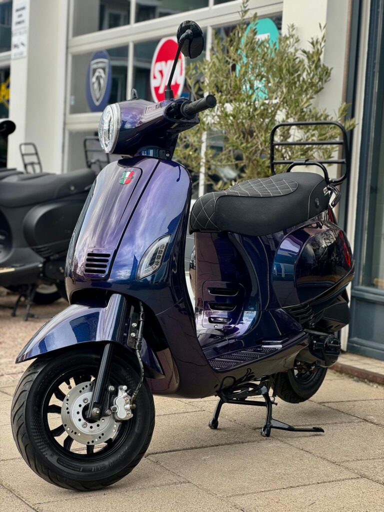 Paarsblauwe retro-scooter op standaard voor een showroom, met ruitpatroon zadel en schijfrem.