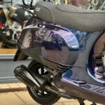 Close-up van de achterzijde van een GTS-scooter met uitlaat en bagagerek, geparkeerd in een showroom.