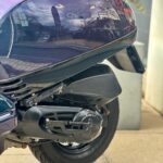 Close-up van de achterzijde van een paarse scooter met motorblok, uitlaat en achterwiel.