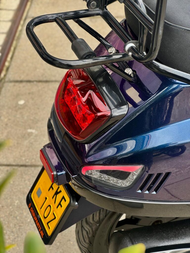 Close-up van de achterkant van een blauw-paarse scooter met bagagerek, achterlicht en gele kentekenplaat.