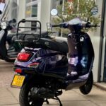 Donkerpaarse scooter met bagagedrager, achteraanzicht voor een winkelpui.