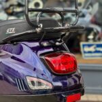 Achterkant van een paarse Vespa GTS-scooter met bagagedrager, achterlicht en knipperlichten.