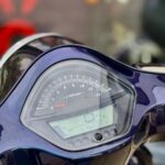 Close-up van een scooter- of motordashboard met toerenteller en digitaal display in een donkerblauwe kuip.