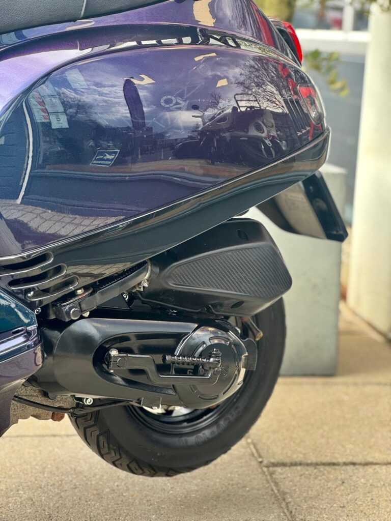 Close-up van de achterzijde van een paarse scooter met motorblok, uitlaat en achterwiel.