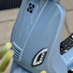 Close-up van de voorkant van een lichtblauwe scooter met koplamp en LED-knipperlicht.