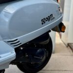 Close-up van de achterzijde van een lichtblauwe agm VX50 scooter met wiel en uitlaat op stoeptegels.