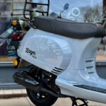 Lichtgrijze AGM VX50 scooter op middenstandaard voor een winkelraam