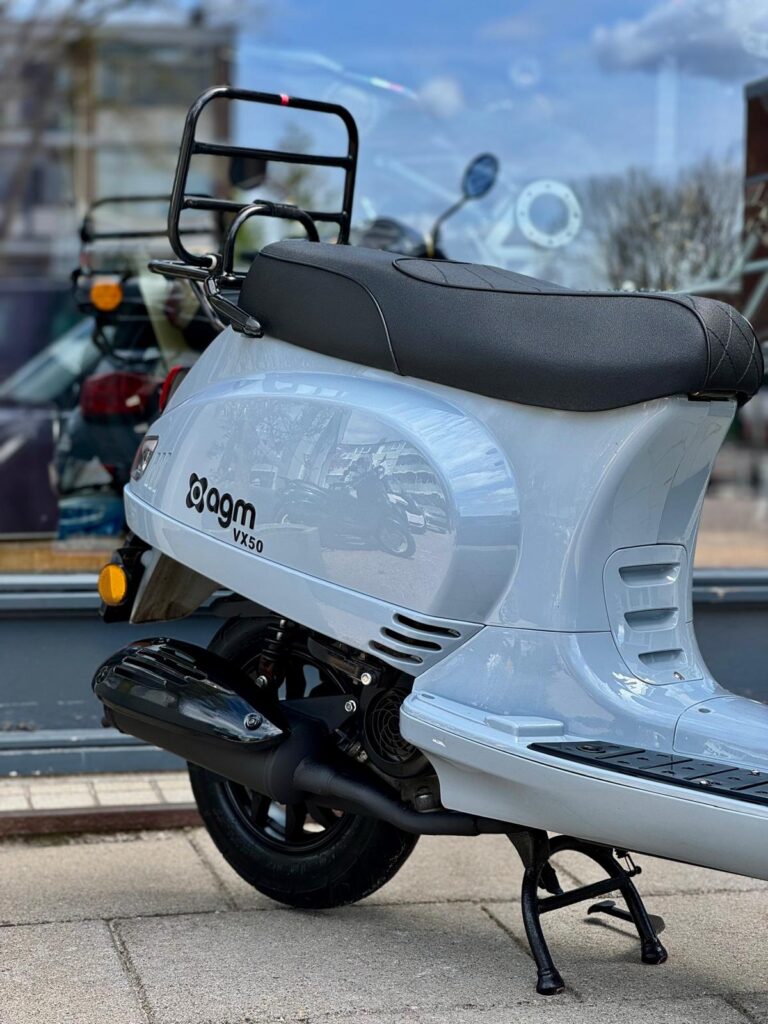 Lichtgrijze AGM VX50 scooter op middenstandaard voor een winkelraam