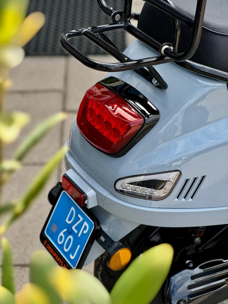 Close-up van de achterkant van een lichtblauwe scooter met bagagedrager, achterlicht en blauwe kentekenplaat.
