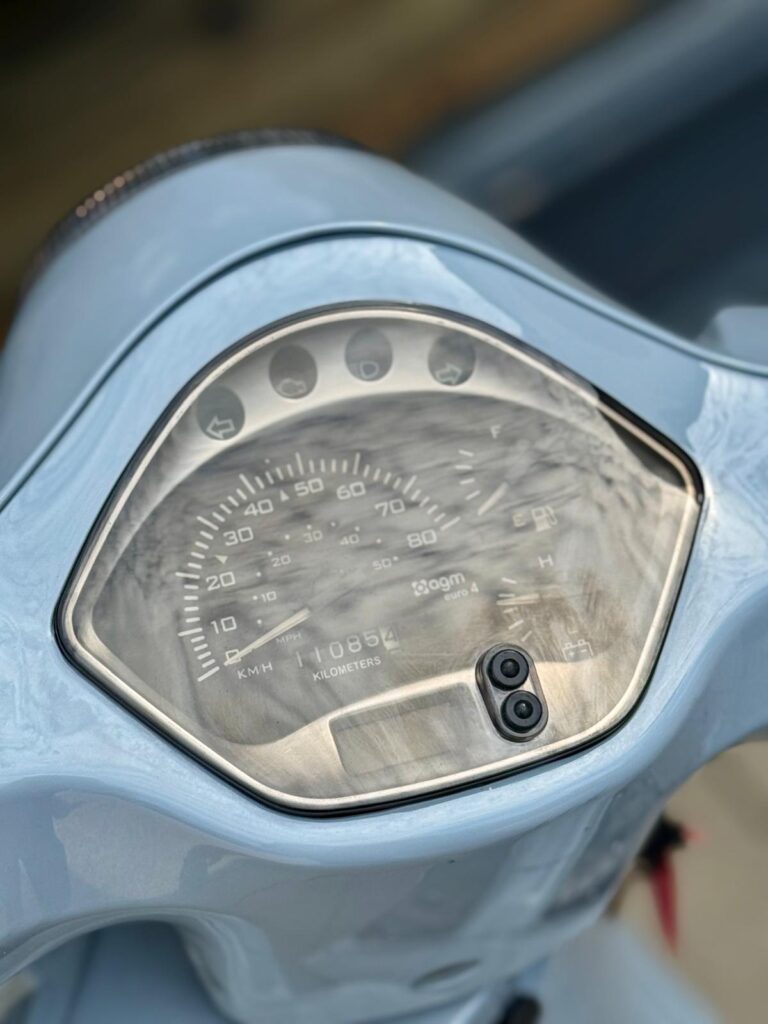 Close-up van de kilometerteller en het dashboard van een lichtblauwe scooter.