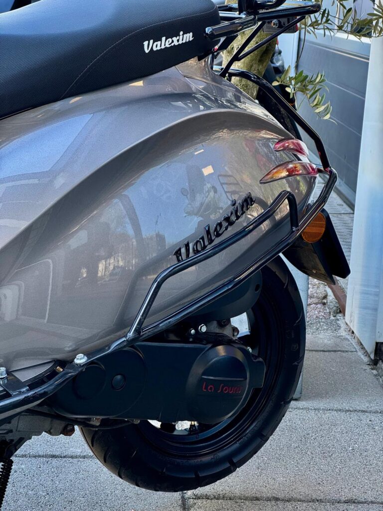 Close-up van de achterzijde van een grijze scooter met Valexim-zadel, achterlicht en achterwiel.