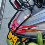 Achterkant van een grijze scooter met bagagedrager, achterlicht en geel kenteken.