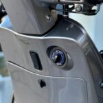 Close-up van het contactsleutelslot en stuurbediening van een grijze scooter.