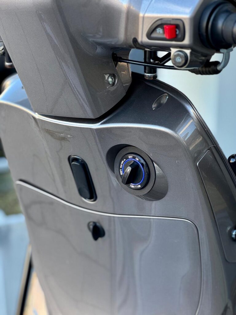 Close-up van het contactsleutelslot en stuurbediening van een grijze scooter.