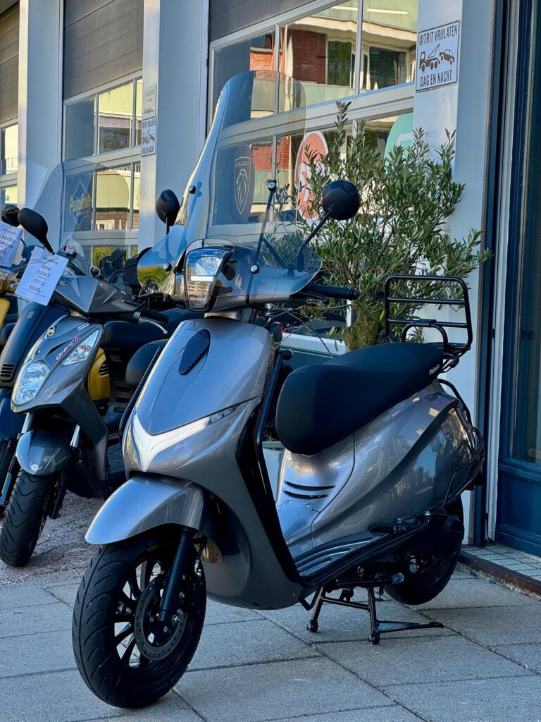Grijze scooter met hoog windscherm op standaard voor een showroom, met andere scooters ernaast.