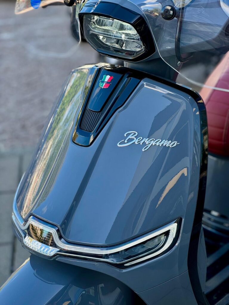 Close-up van de voorkant van een blauwe Bergamo-scooter met LED-koplampen en windscherm.