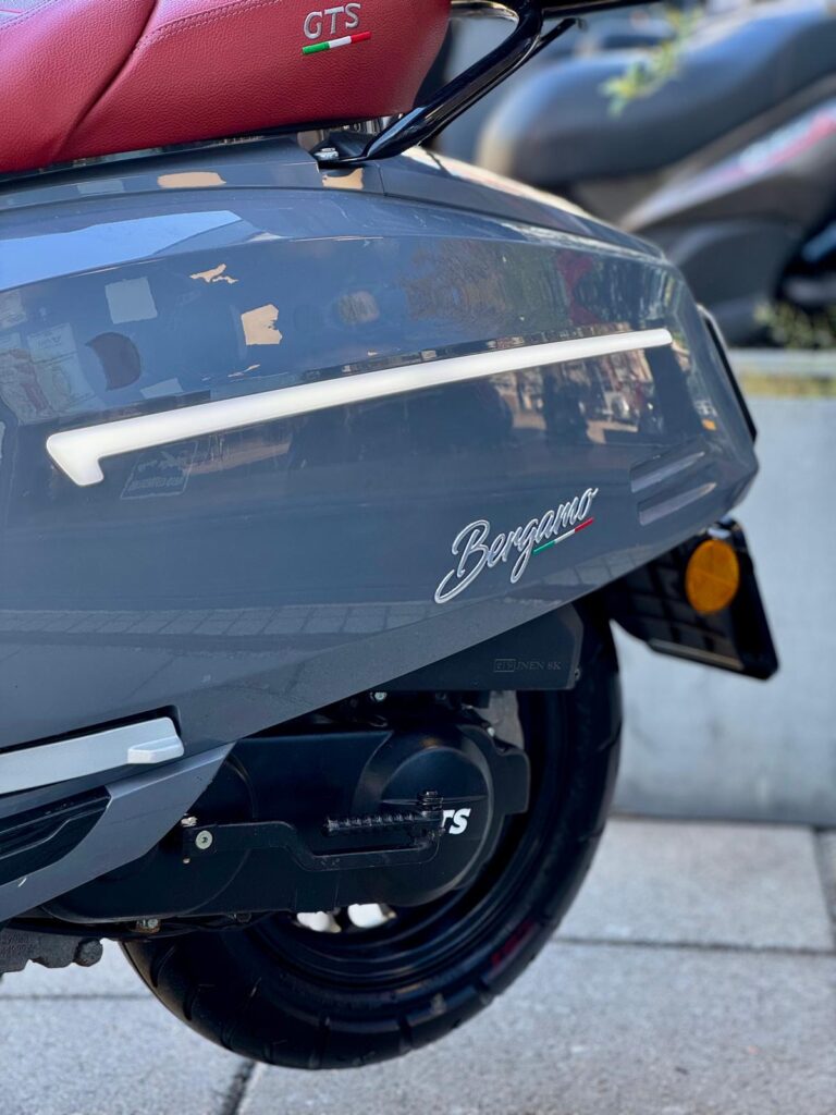 Close-up van de zijkant van een grijze Bergamo-scooter met rood GTS-zadel en zichtbaar achterwiel.