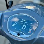 Close-up van scooterdashboard met digitaal display, 0 km/u, 4672 km en bijna lege tank.