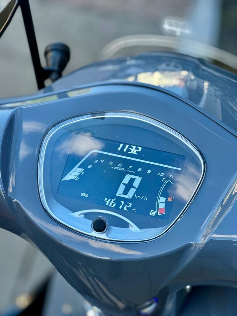 Close-up van scooterdashboard met digitaal display, 0 km/u, 4672 km en bijna lege tank.