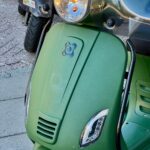 Detail van matgroene scooter met koplamp, knipperlichten en windscherm