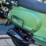 Close-up van een groene scooter, achterzijde met uitlaat, zadel en bagagedrager.