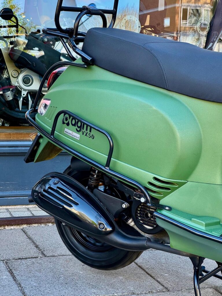 Close-up van een groene scooter, achterzijde met uitlaat, zadel en bagagedrager.