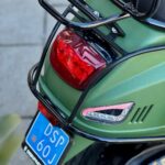 Achterkant van een matte groene scooter met bagagedrager, achterlicht en blauw kenteken.