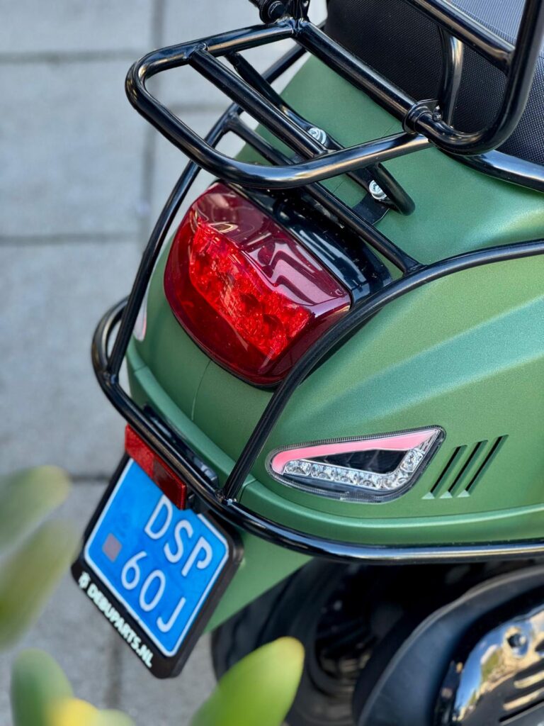 Achterkant van een matte groene scooter met bagagedrager, achterlicht en blauw kenteken.