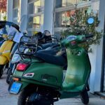 Matgroene retro scooter met bagagedrager en windscherm voor een scootershop.