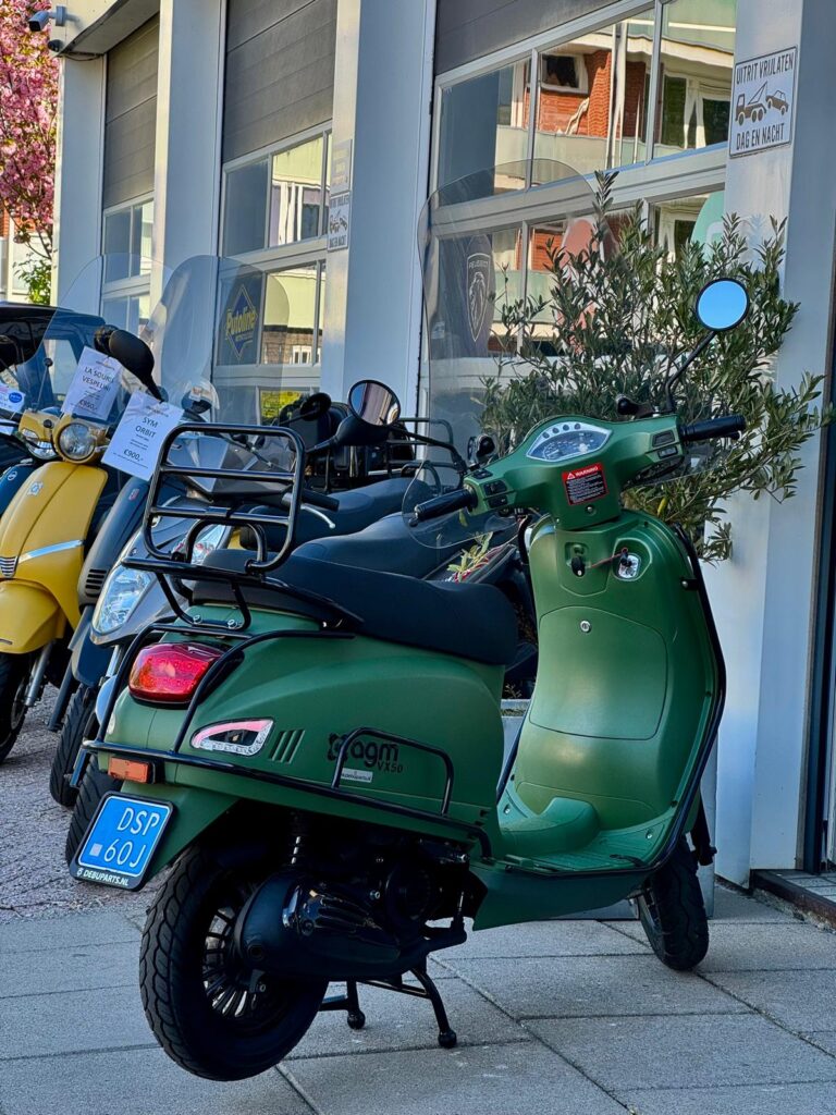 Matgroene retro scooter met bagagedrager en windscherm voor een scootershop.