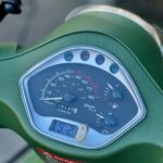 Close-up van het dashboard van een groene scooter met snelheidsmeter, brandstof- en temperatuurmeters.