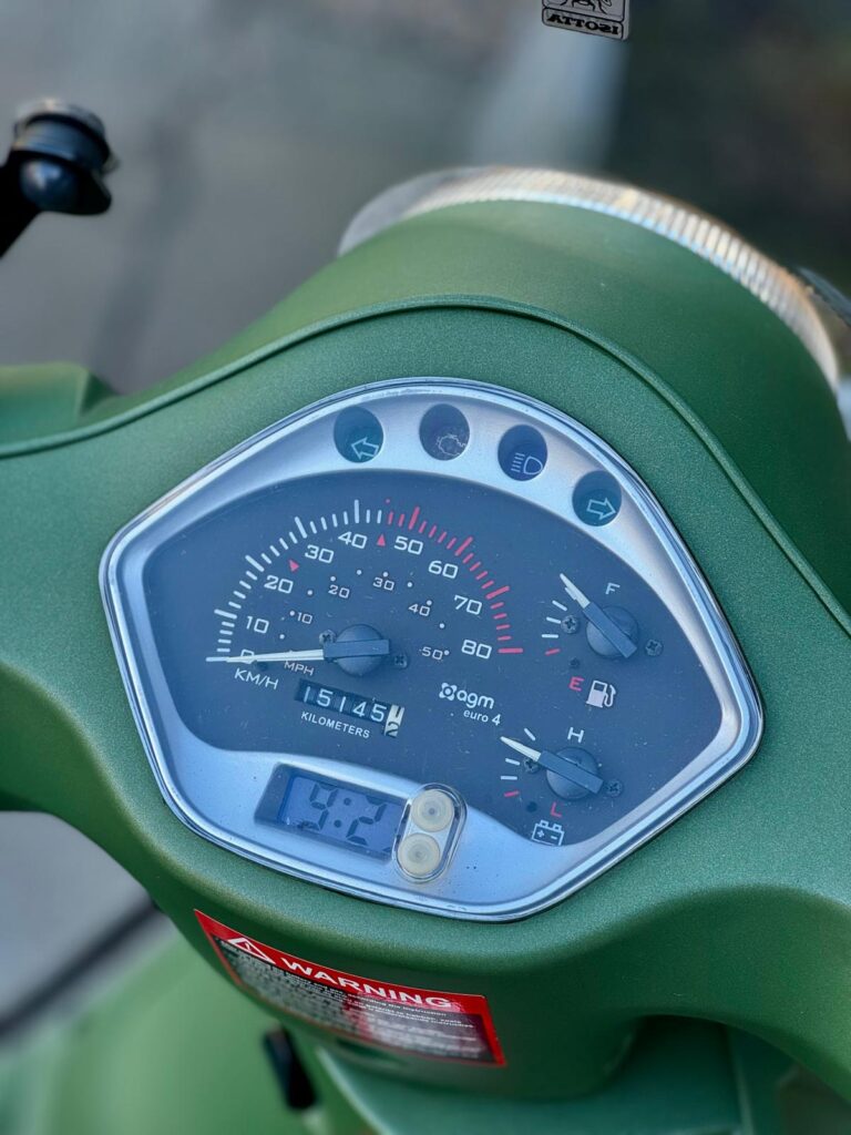 Close-up van het dashboard van een groene scooter met snelheidsmeter, brandstof- en temperatuurmeters.
