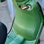 Detail van groene scooter: voetplaat, opbergvak en contactslot met label.