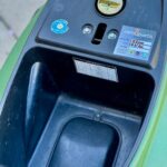 Close-up van scooteropbergruimte onder het zadel met brandstofdop en onderhoudssticker.